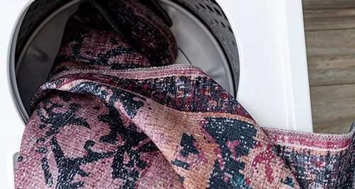 Photo of a washable rug being stuffed into a washing machine.